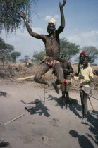 Dinka tribesman with his body painted with ash leaping in to air with his arms held in the shape of the horns of a bull during dance Indigenous