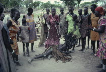 Dinka Binzar or witch doctor wearing head-dress of feathers on ground in trance surrounded by tribeswomen.
