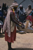 Nigerian woman with child in sling on her back winnowing grain.