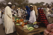 Fruit and vegetable stall at outside market with vendors and male customer.