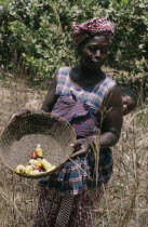 Woman with baby on back holding basket of  cashew fruit with nut