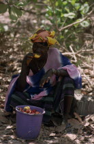 Woman sat  with bucket eating cashew fruit