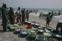 Fishing village with people on the beach with buckets of  the days catch of fish and boats on shoreline.