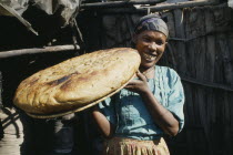 Smiling woman holding up large  circular loaf of bread.aka Nazret  Adaama
