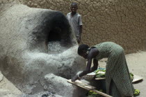 Girl making bread using outside clay oven.