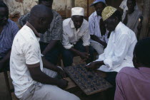 Group of men playing board game of mweso in the street.  A type of mancala also known as omweso or mbao using an 8x4 board.
