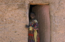 Young girl looking out of doorway of mud brick building.