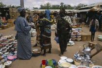 Busy market scene with group of women looking at cooking utensils and pots in the foreground.