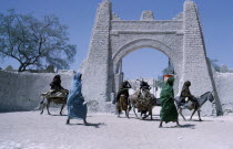 Town gate with women walking or riding donkeys past below.