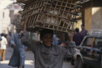 Smiling baker s boy delivering the morning bread carried in basket on his head.