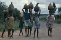 Group of young girls returning from fetching water and carrying gourds on their heads.