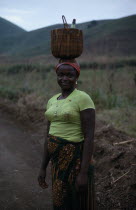 Portrait of young woman carrying woven basket on her head.