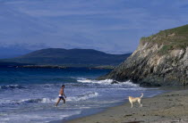 Beach with man walking out of surf towards a dog on the sandEire Republic Eire Republic Eire Republic Eire Republic Eire Republic