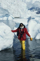 A tourist with camera stands in the water next to icebergs in Waterboat  Point.