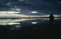 Silhouette of person holding fishing pole with dark sky reflected in the water.