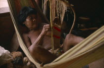 A woman laying in a hammock weaving a piece of material. Brasil