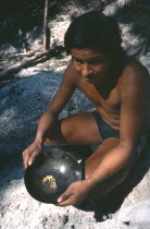 A Tukano Indian crouched down holding a pan of pure gold. Brasil