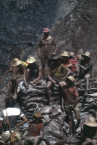 A group of workers covered in mud  sat on sacks of earth  at the biggest hand dug hole  known as the cava  digging for gold.  Brasil