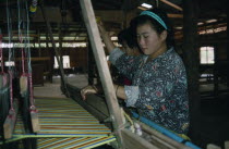 Two women working at a loom at a clothing factory. Burma
