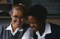 Black and white schoolgirls sharing a joke in the classroom. mixed racemulti cultural African Kids Learning Lessons Teaching