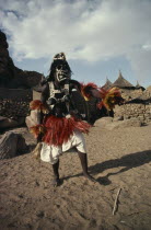 Portrait of Dogon dancer wearing costume of short fringed red and yellow skirt  false breasts and mask decorated with cowrie shells.