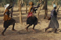 Dogon funeral dance.  Dancers carrying rifles leaping in line.