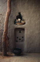 Detail of mud brick house near Kayes with bowl and basket in niche in wall and cooking pot on ground outside.