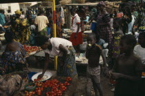 Busy market scene with brightly dressed women and children amongst food stalls.