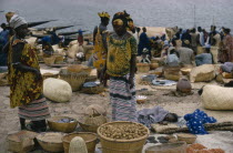 Women traders with baskets of goods and sleeping child at market.