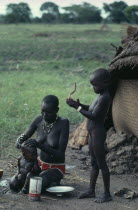 Dinka mother washing her baby with older daughter standing beside her.