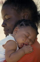 Portrait of young mother holding baby girl asleep on her shoulder with thumb in her mouth.