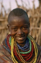 Portrait of Karamojong woman wearing multiple coloured bead necklaces.  Her hair style indicates her clan. Colored