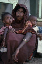 Portrait of young mother with nose ring and facial scarification holding child.