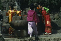 Children wearing traditional national dress drinking from well.