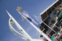 The Spinnaker Tower the tallest public viewing platforn in the UK at 170 metres on Gunwharf Quay with people sitting at tables outside waterfront restaurants