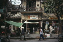 City Old Quarter street scene with roadside vendors  pedestrians and bicycle on balcony of delapidated old colonial building above.