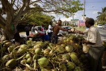 Man buying from men opening coconuts to sell the juice in bottles beside the road in Holetown
