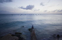 Man on jetty at Half Moon Fort looking out to moored fishing boats at sunset