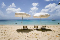 Sun shade umbrellas and chairs on Gibbes Beach with people swimming in the calm sea