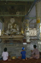 Woman and children kneeling in front of giant seated Buddhist figure. Burma