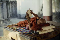Buddhist monk lying on raised platform and reading in Shwedagon Pagoda.Burma Rangoon Shwe Dagon