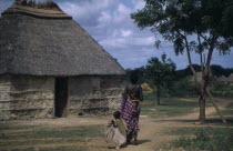 Woman and child walking towards traditional thatchedhouse near Baidoa.