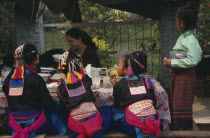 Hmong girls in traditional dress eating at roadside foodstall.