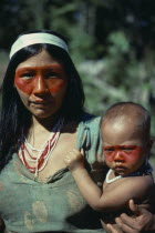 Auca Indian woman holding baby both decorated with red face paint from the achole plant.Waorani