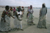 Settled nomad women mending fishing net on shore of beach.