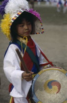Little girl in costume playing drum painted with Taegukki symbol during Childrens Day festivities in May.