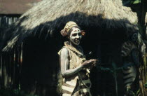Portrait of Kikuya tribeswoman wearing traditional jewellery and body paint standing outside hut.
