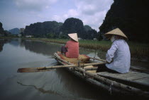 Two women rowing bamboo canoe.