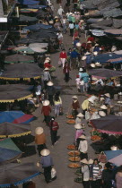 Market scene from above with people in conical hats walking amongst fruit and vegetable sellers with stalls under umbrellas along each side.