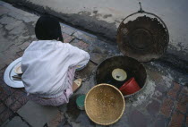 Girl washing pots in a communal water well in the pavement  beside a drain
